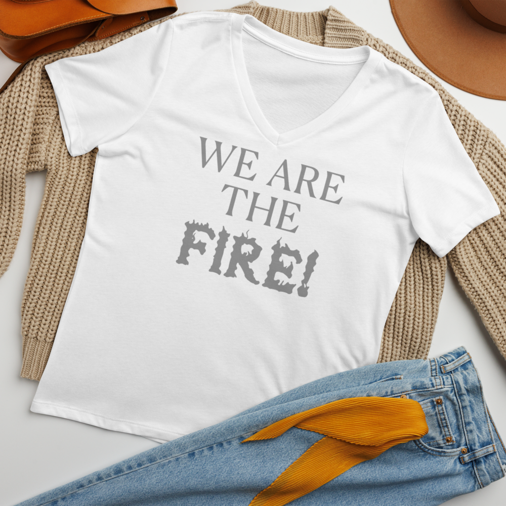 "We are the fire!" printed on a solid white blend women's relaxed v-neck t-shirt laying on a flat surface amongst other clothes
