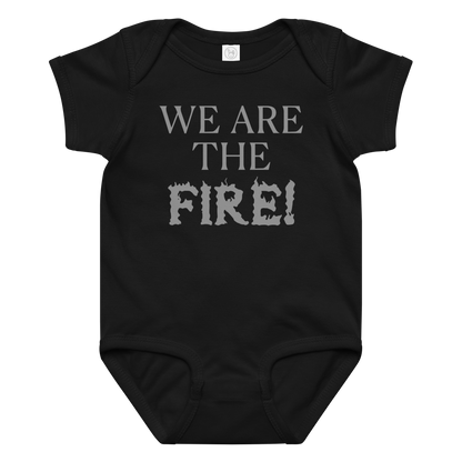 "We are the fire!" printed on a black baby jersey bodysuit laying on a flat surface amongst other clothes