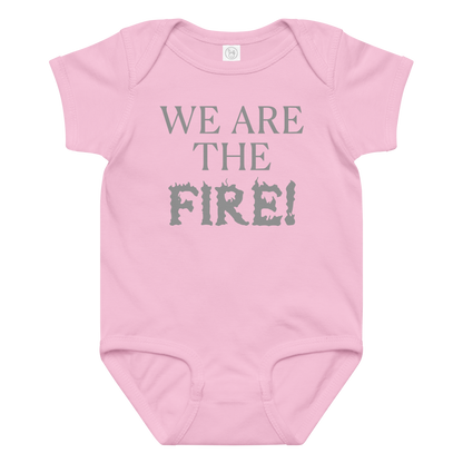 "We are the fire!" printed on a pink baby jersey bodysuit laying on a flat surface amongst other clothes