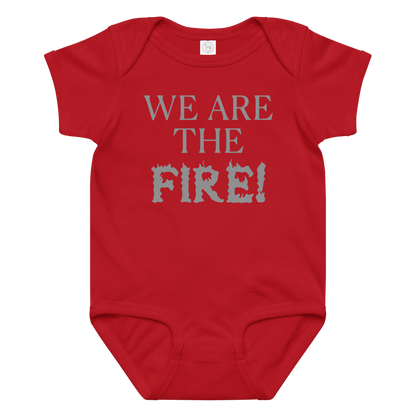 "We are the fire!" printed on a red baby jersey bodysuit laying on a flat surface amongst other clothes