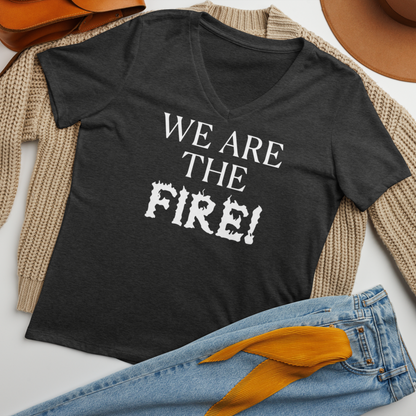 "We are the fire!" printed on a dark grey heather women's relaxed v-neck t-shirt laying on a flat surface amongst other clothes