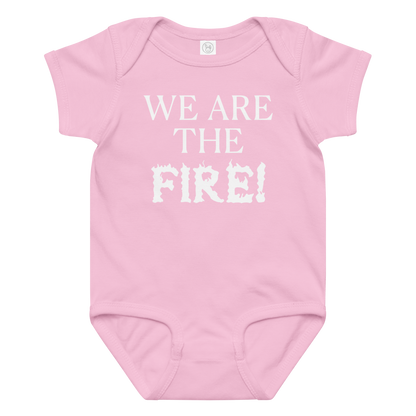 "We are the fire!" printed on a pink baby jersey bodysuit laying on a flat surface amongst other clothes