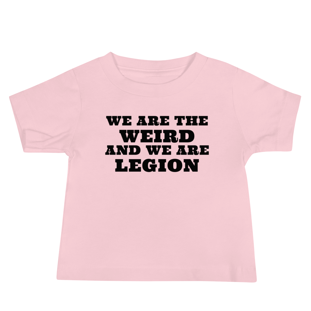 "We are the weird and we are legion" printed on a pink baby jersey short sleeve tee laying on a flat surface