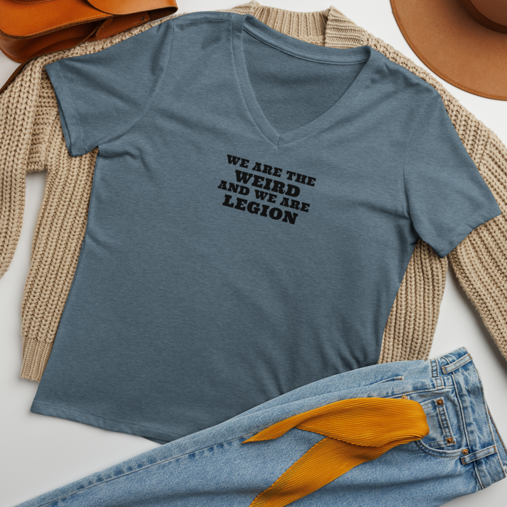"We are the weird and we are legion" printed on a heather slate women's relaxed v-neck t-shirt laying on a flat surface amongst other clothes