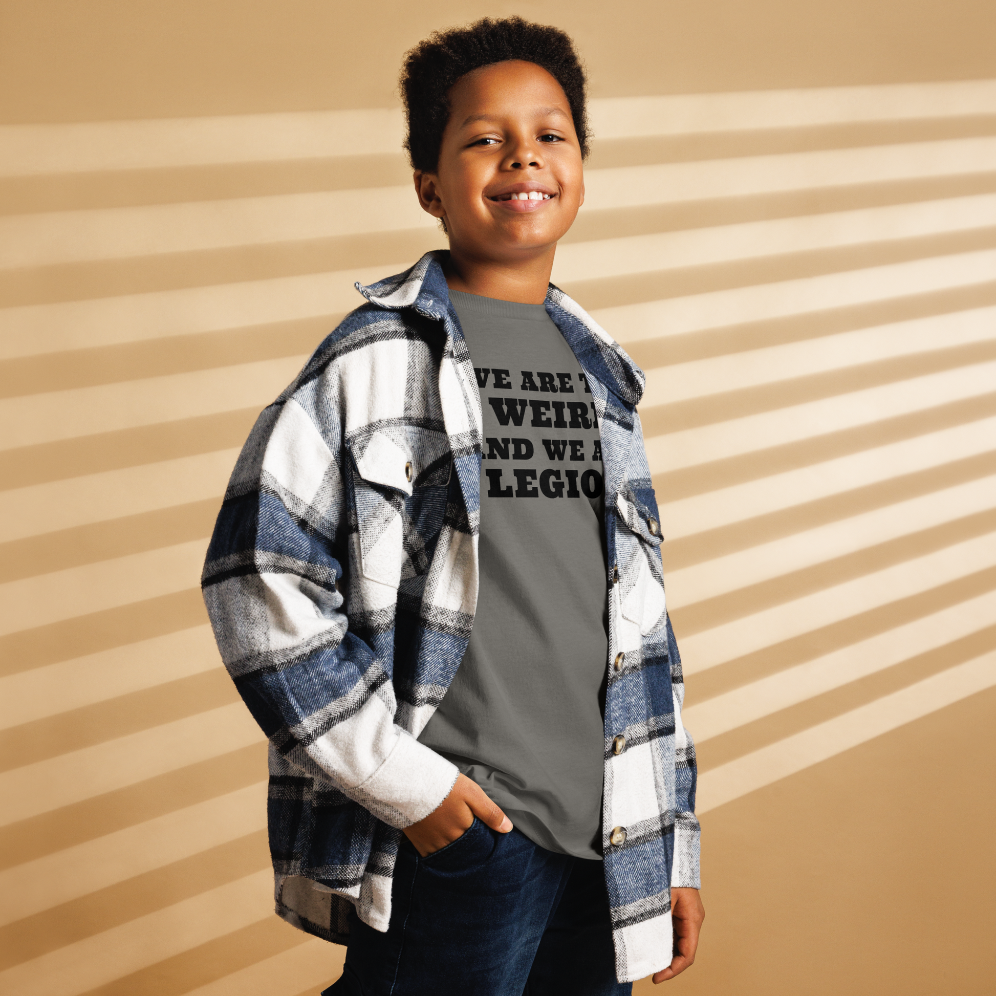 "We are the weird and we are legion" printed on a charcoal youth classic tee worn by a male also wearing a jacket