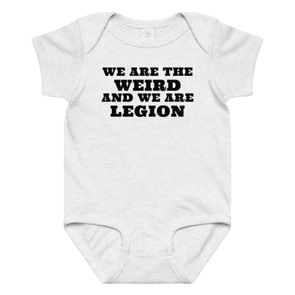 "We are the weird and we are legion" printed on a ash baby jersey bodysuit laying on a flat surface amongst other clothes