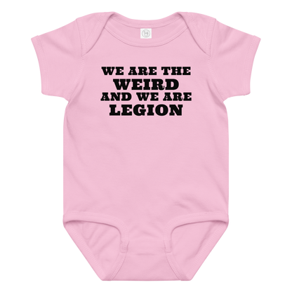"We are the weird and we are legion" printed on a pink baby jersey bodysuit laying on a flat surface amongst other clothes