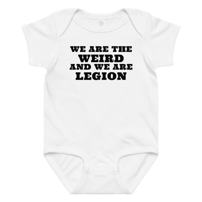 "We are the weird and we are legion" printed on a white baby jersey bodysuit laying on a flat surface amongst other clothes