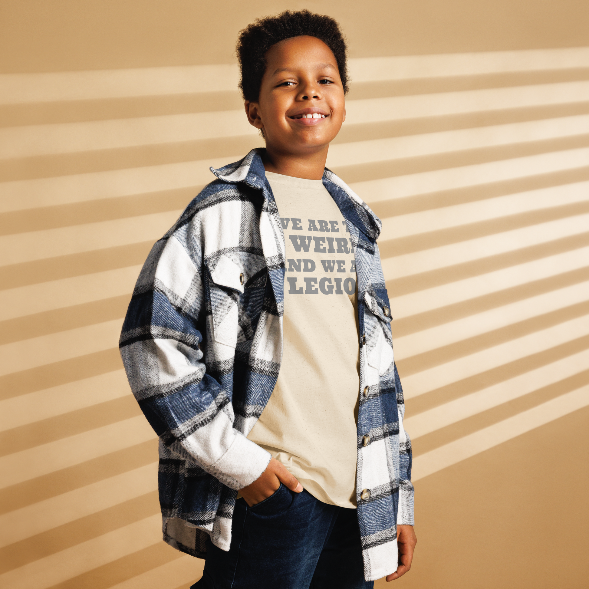 "We are the weird and we are legion" printed on a natural youth classic tee worn by a male also wearing a jacket