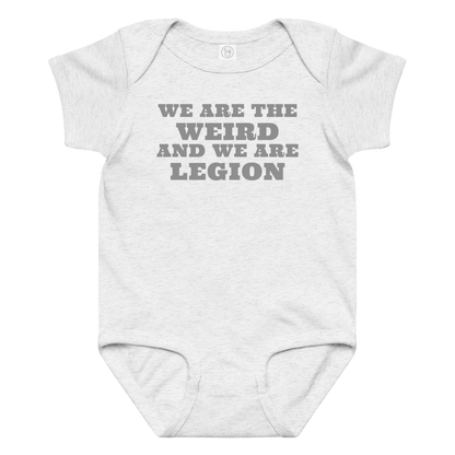 "We are the weird and we are legion" printed on a ash baby jersey bodysuit laying on a flat surface amongst other clothes
