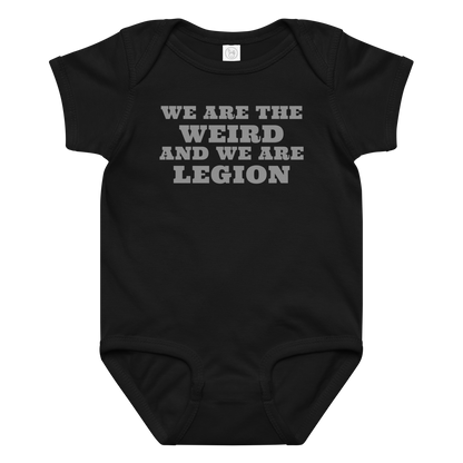 "We are the weird and we are legion" printed on a black baby jersey bodysuit laying on a flat surface amongst other clothes
