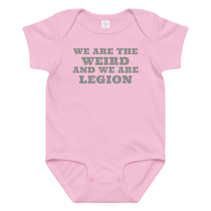 "We are the weird and we are legion" printed on a pink baby jersey bodysuit laying on a flat surface amongst other clothes