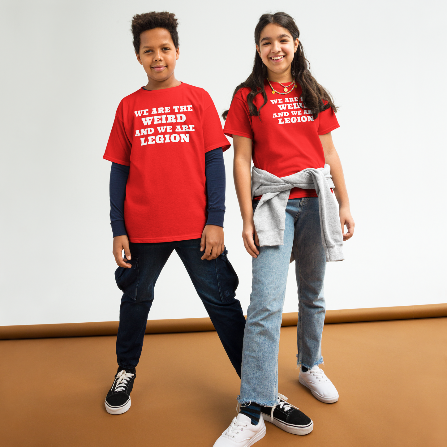 "We are the weird and we are legion" printed on a red youth classic tee worn by a female and male