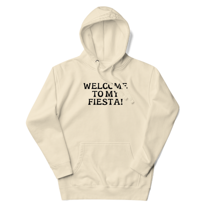 "Welcome to my fiesta!" printed on a bone unisex hoodie laying on a flat surface with the hood up