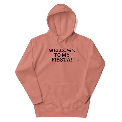 "Welcome to my fiesta!" printed on a dusty rose unisex hoodie laying on a flat surface with the hood up