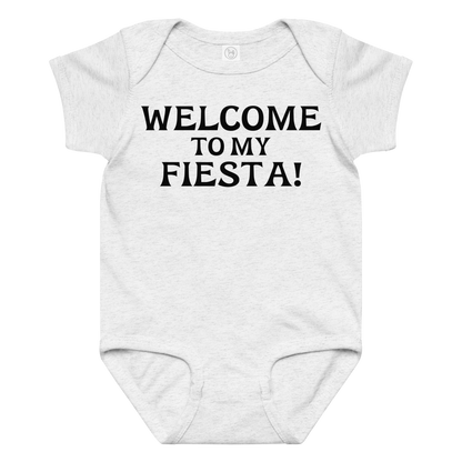 "Welcome to my fiesta!" printed on a ash baby jersey bodysuit laying on a flat surface amongst other clothes