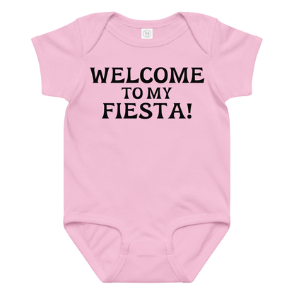 "Welcome to my fiesta!" printed on a pink baby jersey bodysuit laying on a flat surface amongst other clothes