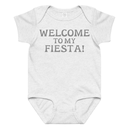 "Welcome to my fiesta!" printed on a ash baby jersey bodysuit laying on a flat surface amongst other clothes