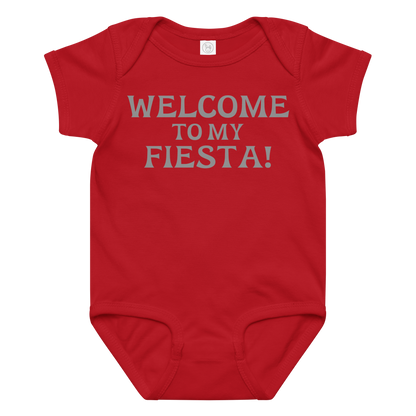 "Welcome to my fiesta!" printed on a red baby jersey bodysuit laying on a flat surface amongst other clothes