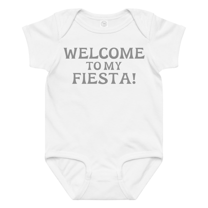 "Welcome to my fiesta!" printed on a white baby jersey bodysuit laying on a flat surface amongst other clothes