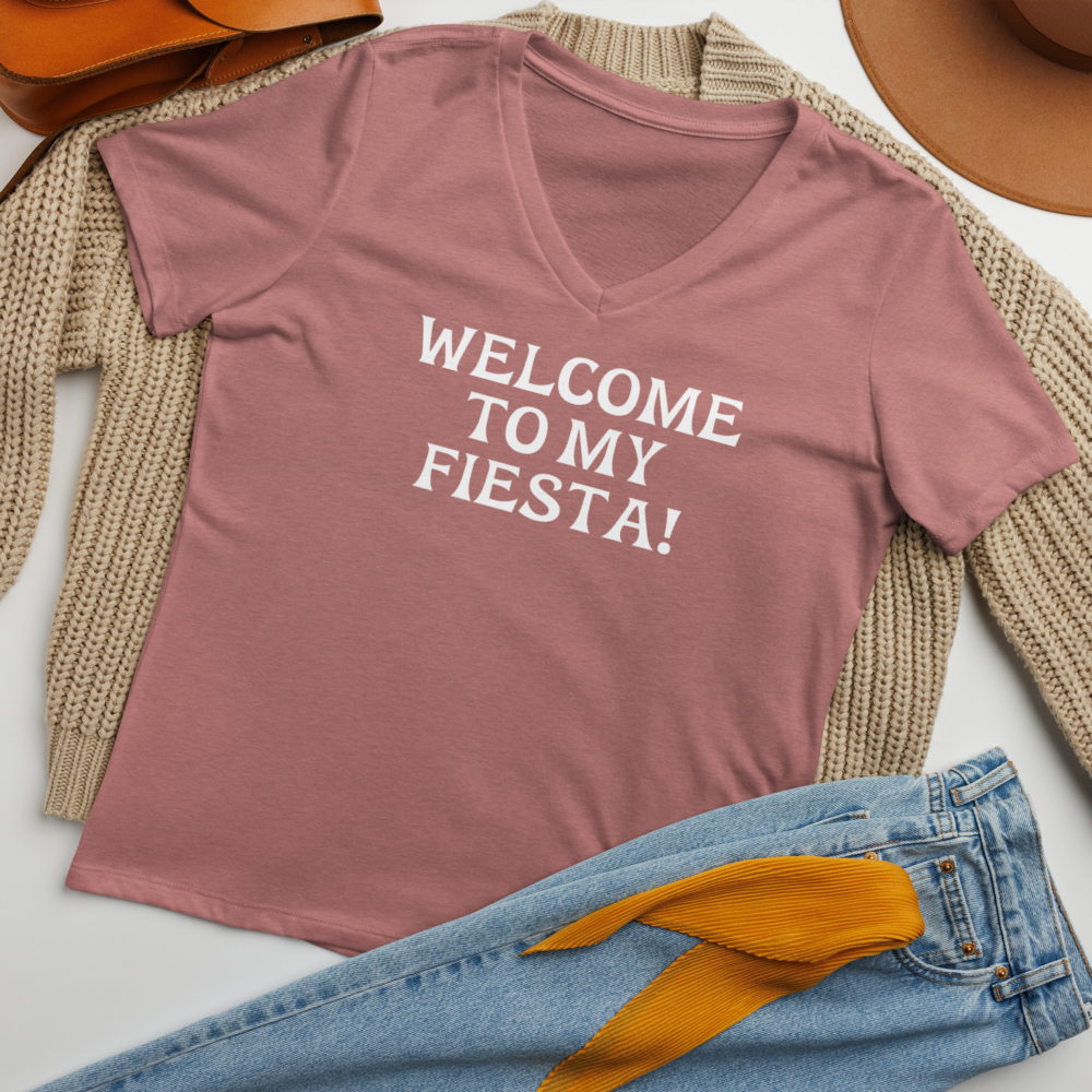 "Welcome to my fiesta!" printed on a heather mauve women's relaxed v-neck t-shirt laying on a flat surface amongst other clothes