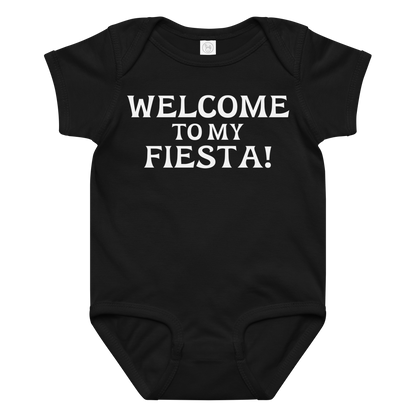 "Welcome to my fiesta!" printed on a black baby jersey bodysuit laying on a flat surface amongst other clothes