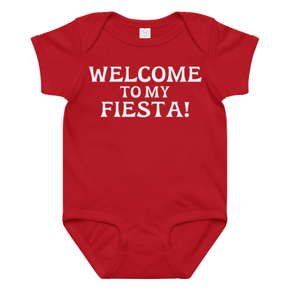 "Welcome to my fiesta!" printed on a red baby jersey bodysuit laying on a flat surface amongst other clothes