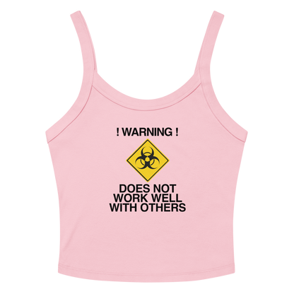 "!Warning! Does Not Work Well With Others" printed on a solid pink blend women's micro-rib tanktop laying on a flat surface amongst sunglasses and shorts