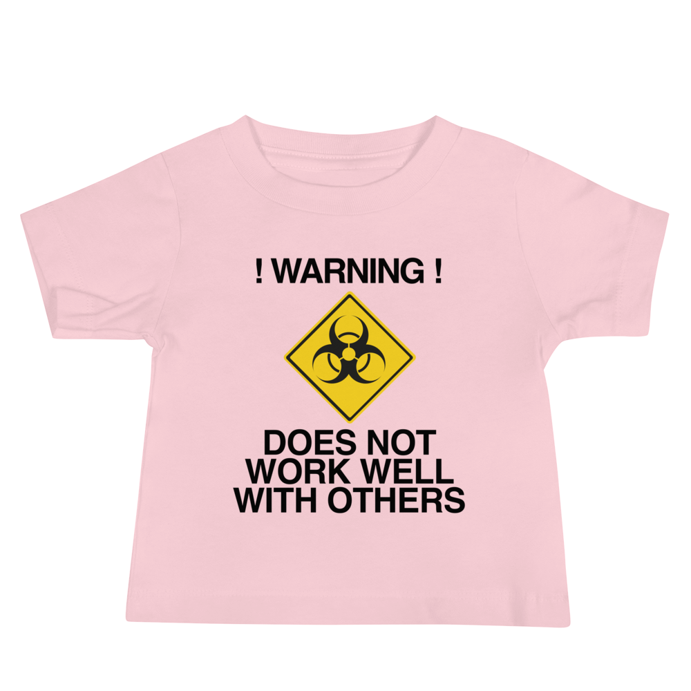 "!Warning! Does Not Work Well With Others" printed on a pink baby jersey short sleeve tee laying on a flat surface