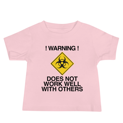 "!Warning! Does Not Work Well With Others" printed on a pink baby jersey short sleeve tee laying on a flat surface