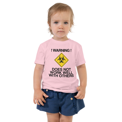 "!Warning! Does Not Work Well With Others" printed on a pink toddler short sleeve tee worn by a female