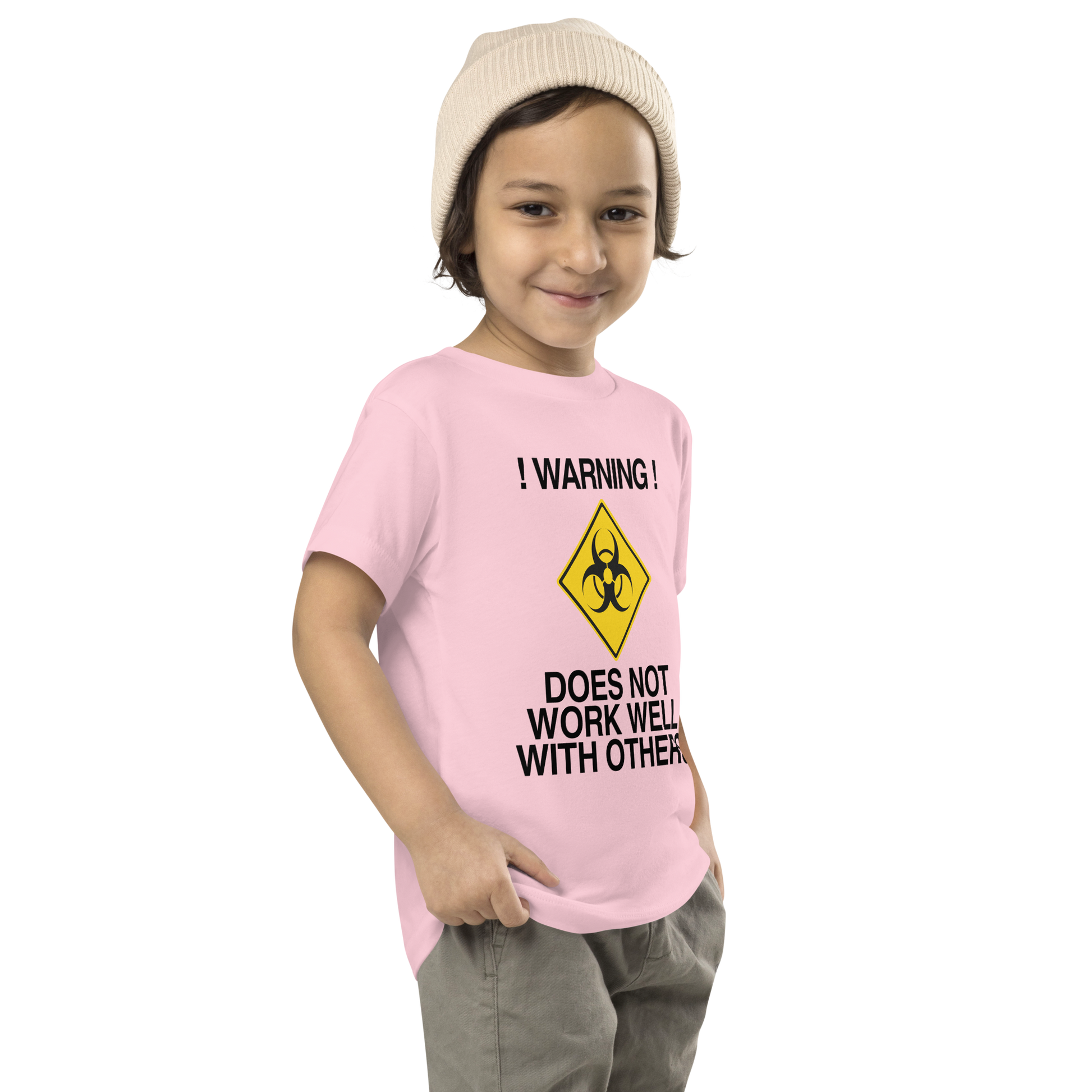 "!Warning! Does Not Work Well With Others" printed on a pink toddler short sleeve tee worn by a male who is also wearing a knit cap