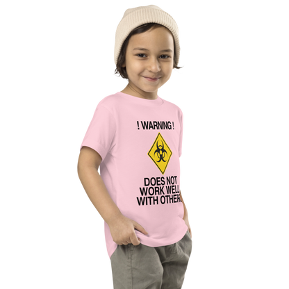 "!Warning! Does Not Work Well With Others" printed on a pink toddler short sleeve tee worn by a male who is also wearing a knit cap