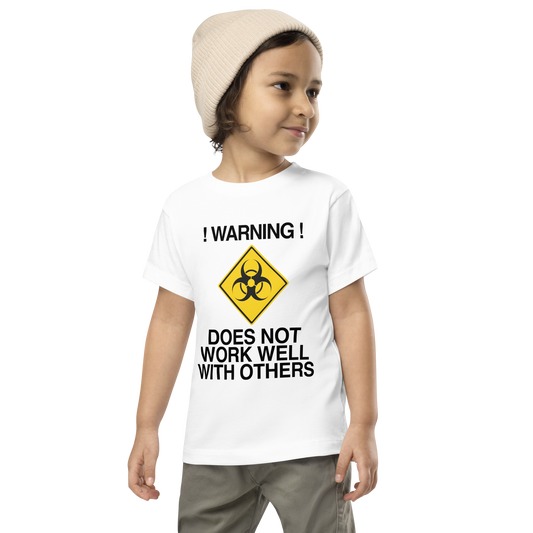 "!Warning! Does Not Work Well With Others" printed on a white toddler short sleeve tee worn by a male wearing a cap