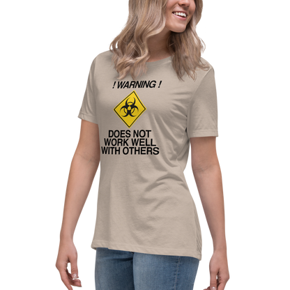 "!Warning! Does Not Work Well With Others" printed on a heather stone women's relaxed t-shirt worn by a female