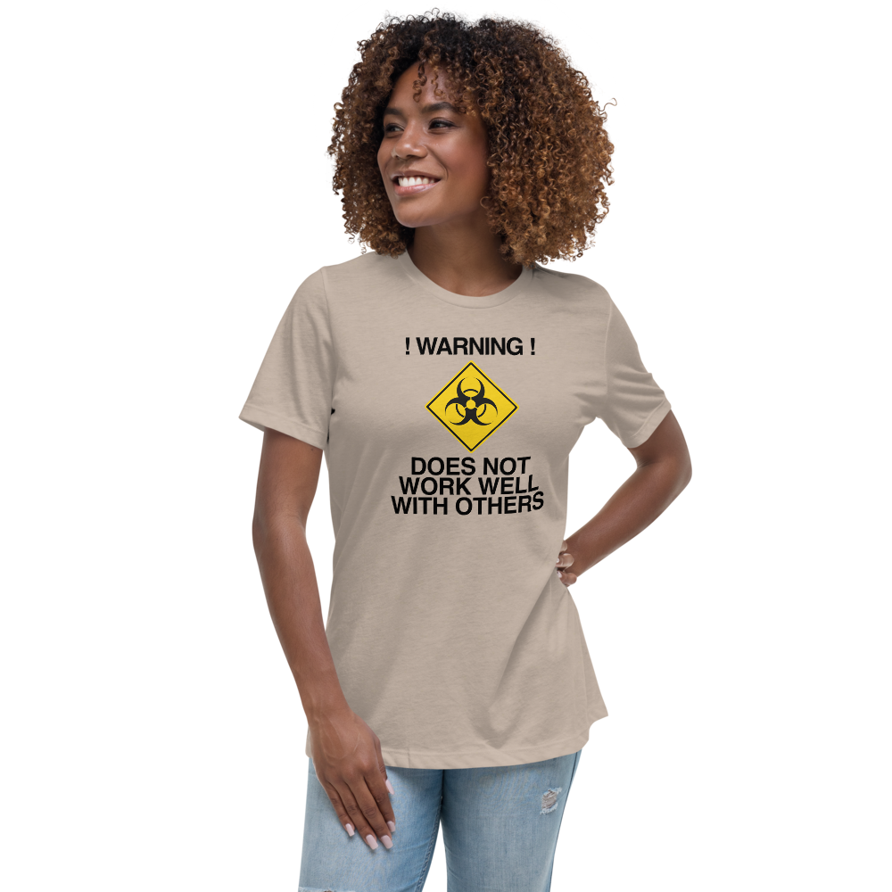 "!Warning! Does Not Work Well With Others" printed on a heather stone women's relaxed t-shirt worn by a female