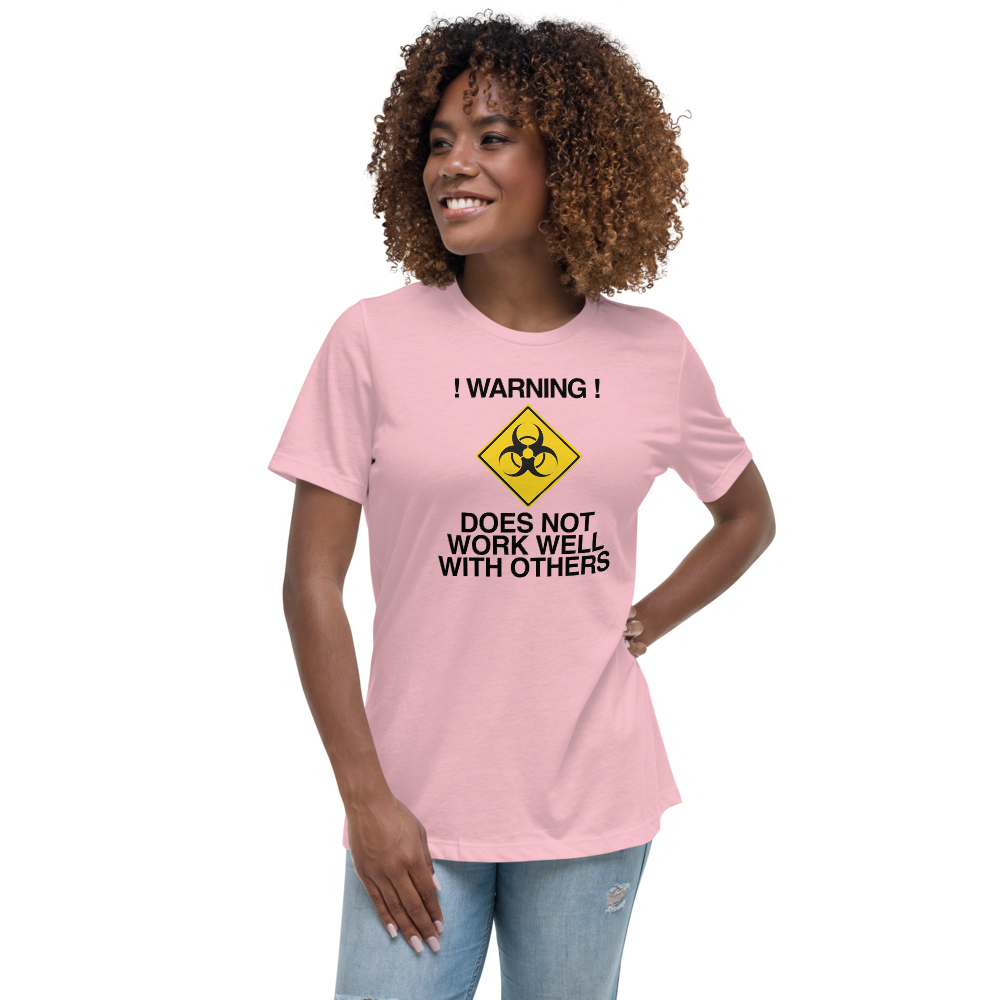 "!Warning! Does Not Work Well With Others" printed on a pink women's relaxed t-shirt worn by a female