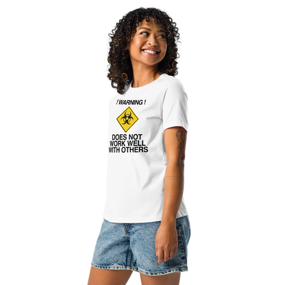 "!Warning! Does Not Work Well With Others" printed on a white women's relaxed t-shirt worn by a female