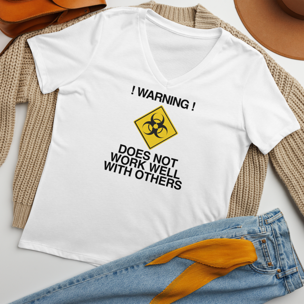 "!Warning! Does Not Work Well With Others" printed on a solid white blend women's relaxed v-neck t-shirt laying on a flat surface amongst other clothes