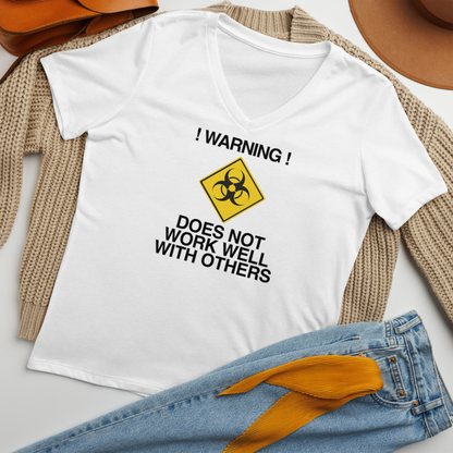 "!Warning! Does Not Work Well With Others" printed on a solid white blend women's relaxed v-neck t-shirt laying on a flat surface amongst other clothes