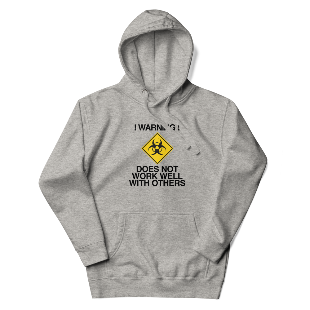 "!Warning! Does Not Work Well With Others" printed on a carbon grey unisex hoodie laying on a flat surface with the hood up