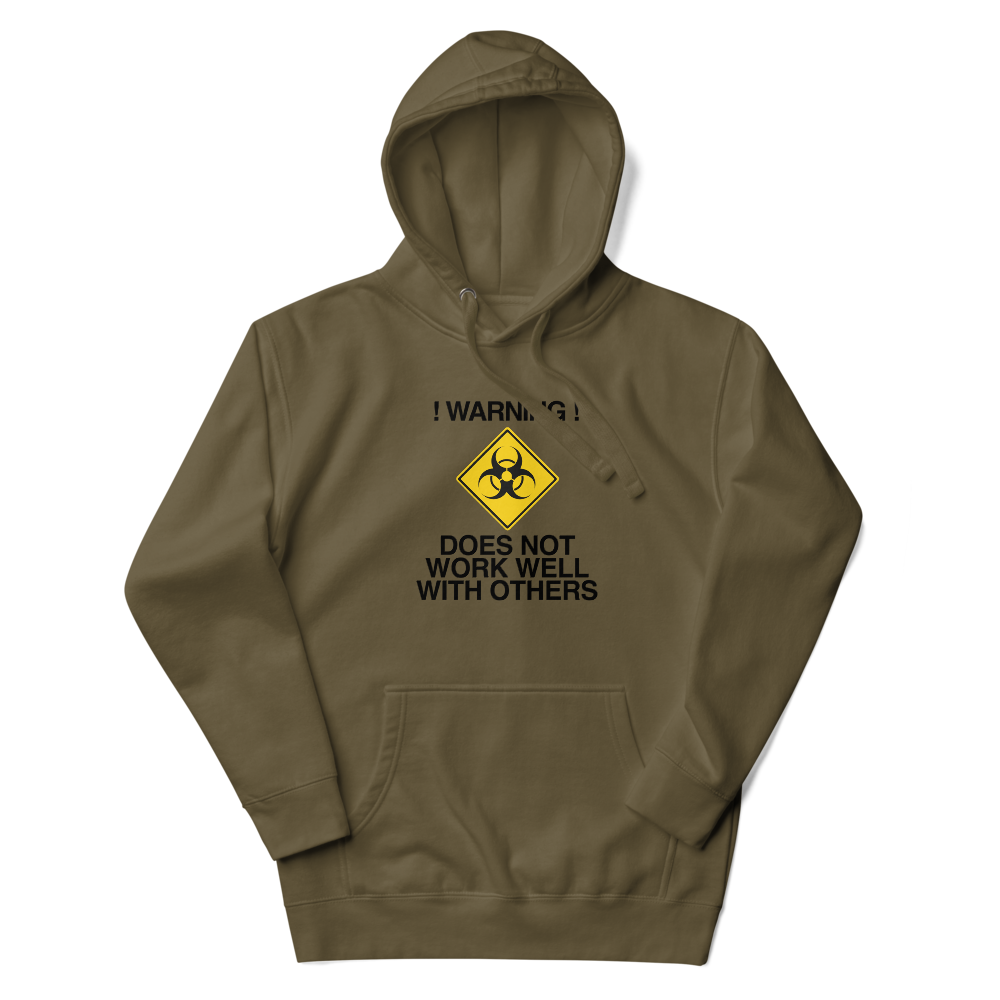 "!Warning! Does Not Work Well With Others" printed on a military green unisex hoodie laying on a flat surface with the hood up