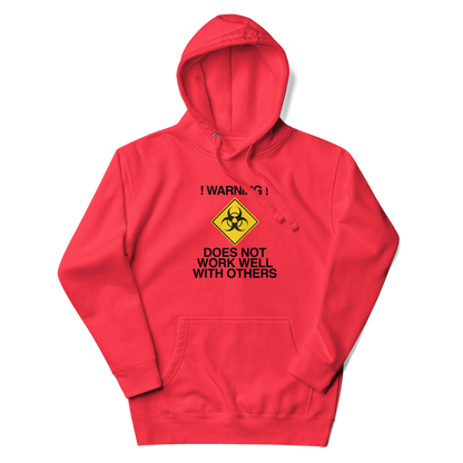 "!Warning! Does Not Work Well With Others" printed on a team red unisex hoodie laying on a flat surface with the hood up