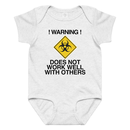 "!Warning! Does Not Work Well With Others" printed on a ash baby jersey bodysuit laying on a flat surface amongst other clothes