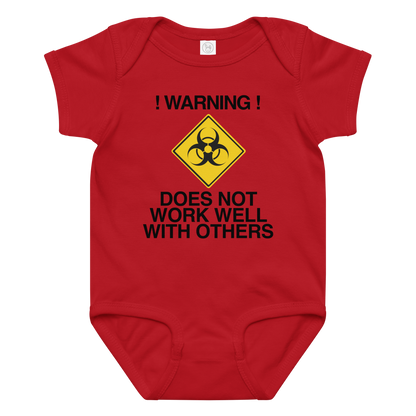 "!Warning! Does Not Work Well With Others" printed on a red baby jersey bodysuit laying on a flat surface amongst other clothes