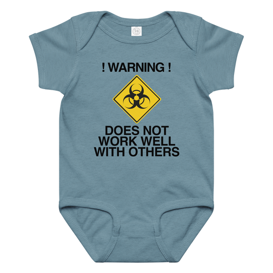 "!Warning! Does Not Work Well With Others" printed on a vintage indigo baby jersey bodysuit laying on a flat surface amongst other clothes