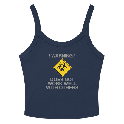 "!Warning! Does Not Work Well With Others" printed on a solid navy blend women's micro-rib tanktop laying on a flat surface amongst sunglasses and shorts