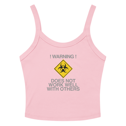 "!Warning! Does Not Work Well With Others" printed on a solid pink blend women's micro-rib tanktop laying on a flat surface amongst sunglasses and shorts