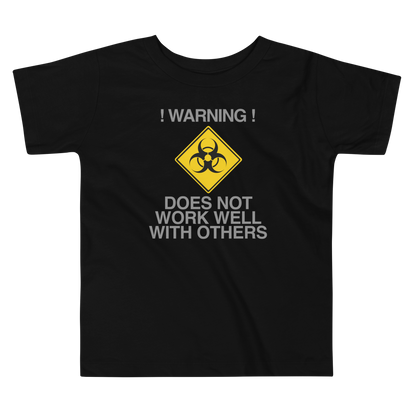 "!Warning! Does Not Work Well With Others" printed on a black toddler short sleeve tee laying on a flat surface