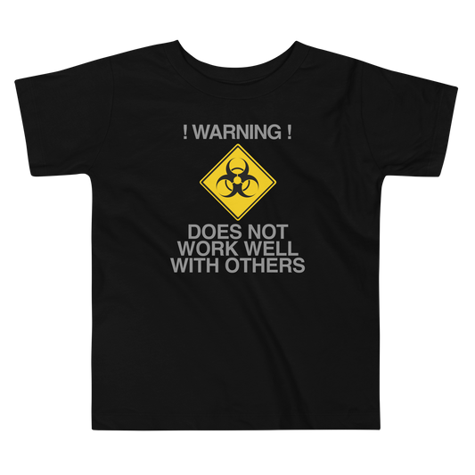 "!Warning! Does Not Work Well With Others" printed on a black toddler short sleeve tee laying on a flat surface